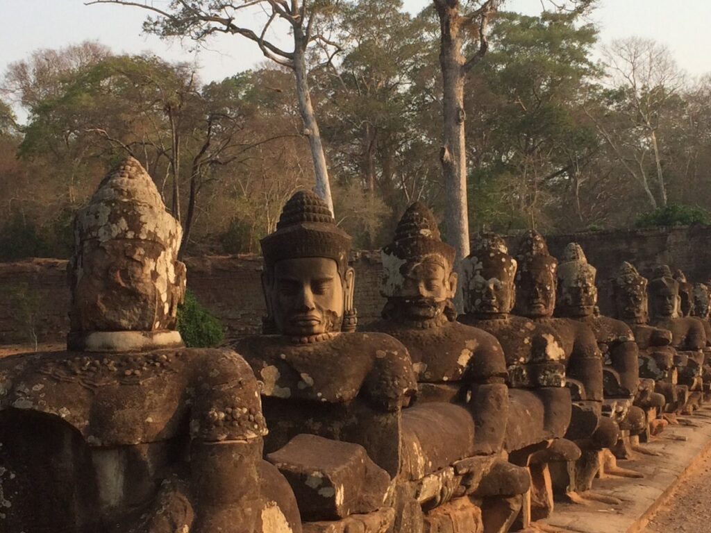 A row of stone statues of male figures sitting in a row with eyes closed in meditation along road and near the entrance to Angkor Wat temple in Cambodia.