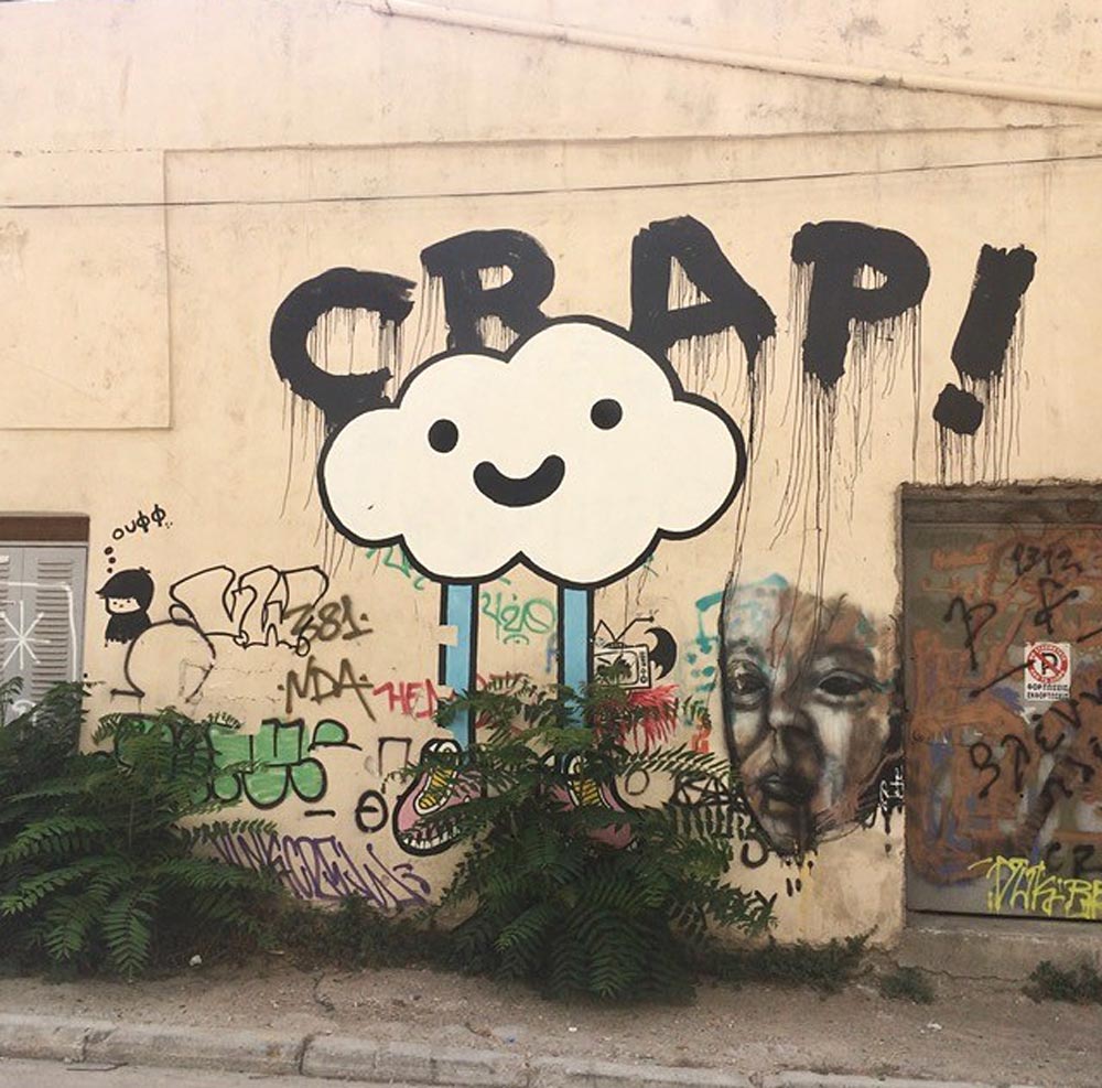 Building wall with various graffiti, including a smiling cloud character and the word "CRAP!" above it.