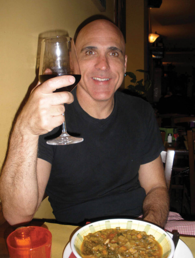 Inner Space host, Ralph Williams, sits in front of a bowl of Tuscan soup while holding a glass of red wine at a restaurant in Florence, Italy.