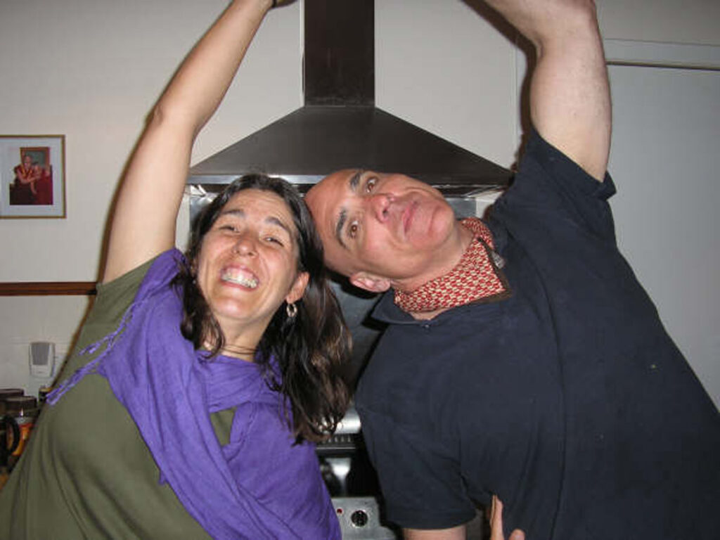 Two people in a kitchen, arms overhead, one smiling broadly, background with range hood and framed picture.