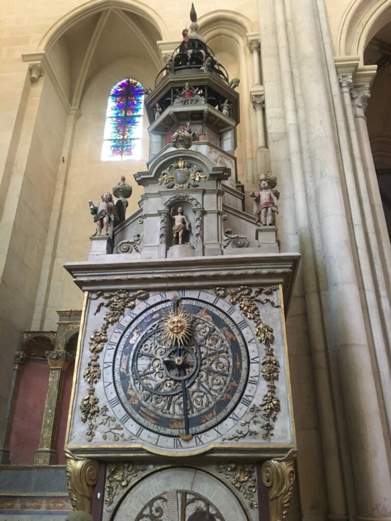 Ornate astronomical clock inside cathedral with Roman numerals, statues, stained glass window.