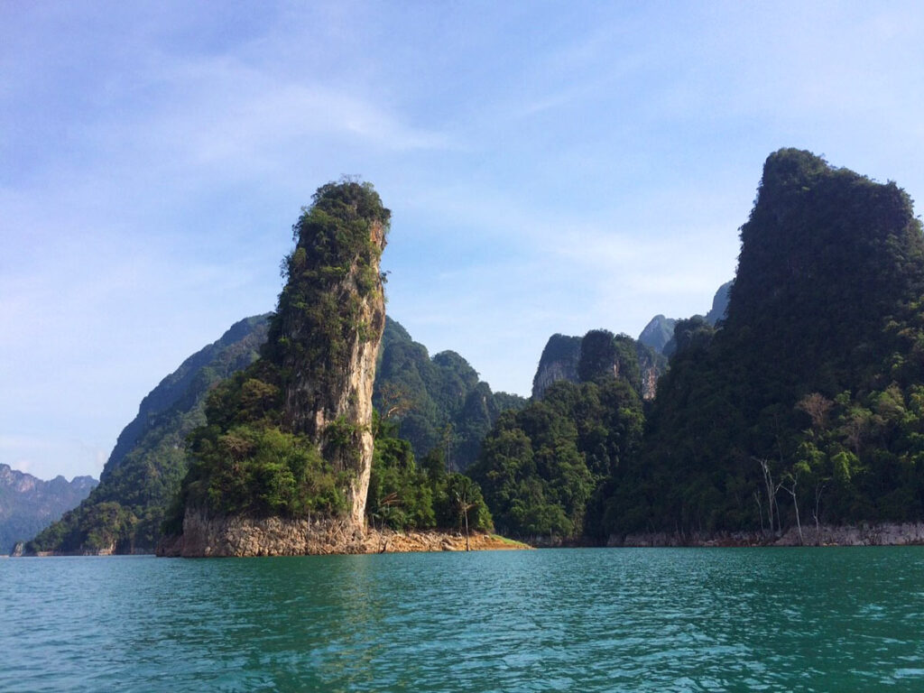 Calm water with forest-covered limestone cliffs and a clear blue sky in the background.