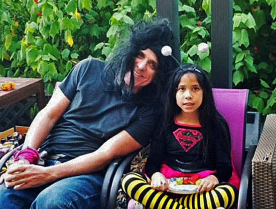 Adult and child in costumes seated outdoors, adult with a black wig, child in superhero outfit.