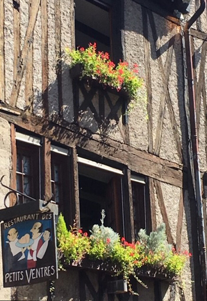 Building's facade with wooden beams, plaster walls, restaurant sign, and flower boxes under windows.