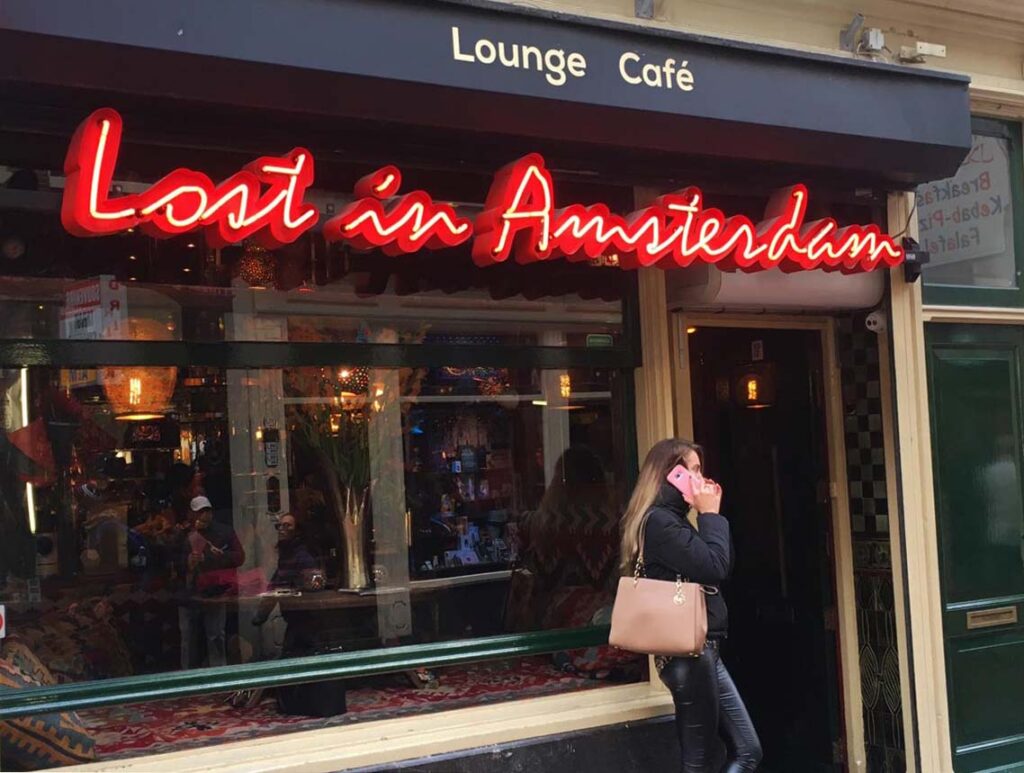 Entrance to the "Lost in Amsterdam" Café with its neon red sign stretched across the front window and a young woman talking on a pink mobile phone.