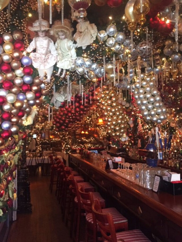 Lavishly decorated festive bar and dining area with ornaments, illuminated garlands, and vintage dolls.