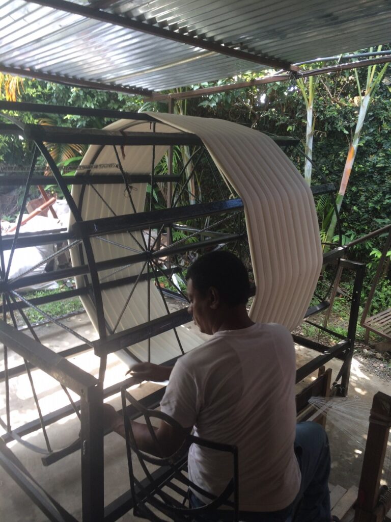 Man working on a metal frame under a corrugated roof in an outdoor workshop.