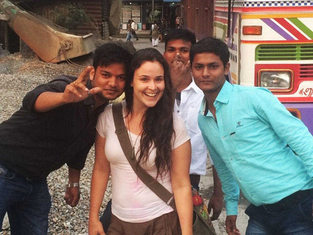 Group of four posing in front of a colorful vehicle at an outdoor site.