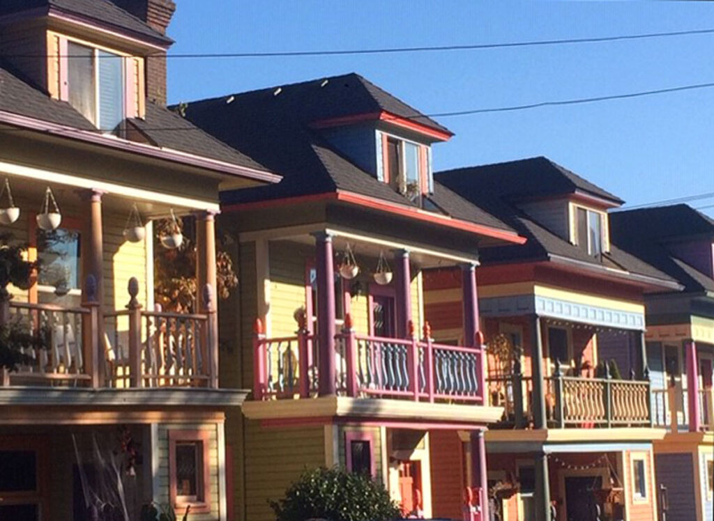 Colorful, two-story homes with front porches and balconies in sunlight.