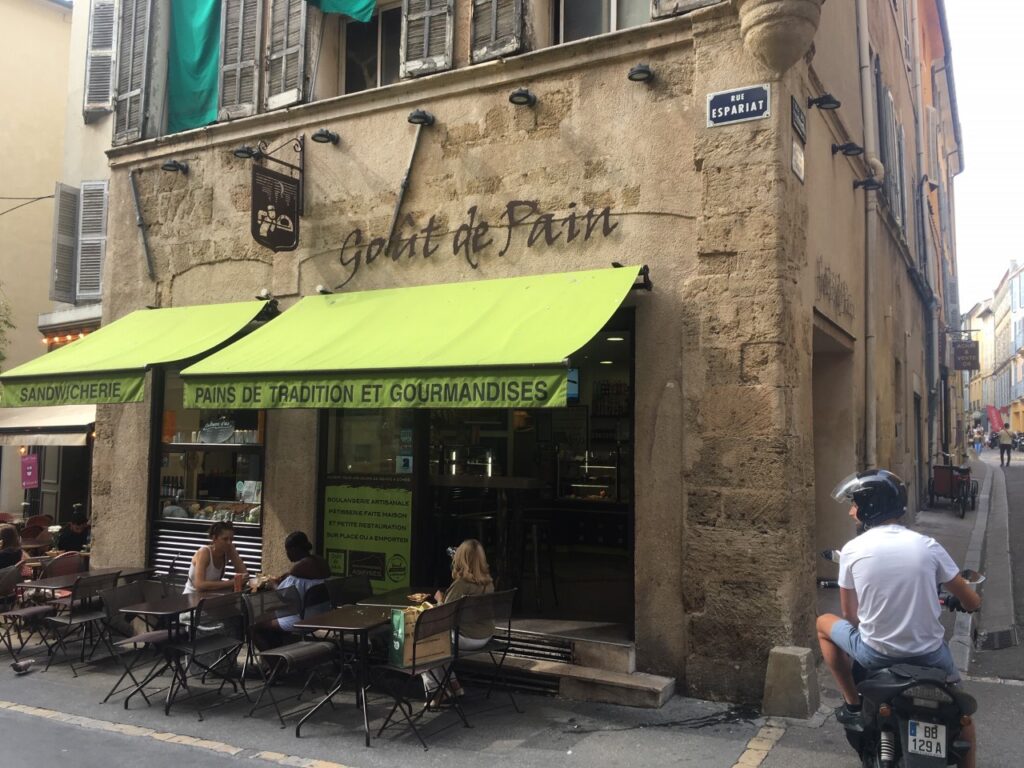 Small bakery and sandwich shop "Goût de Pain" on Rue Espariat with outdoor seating and green awning.