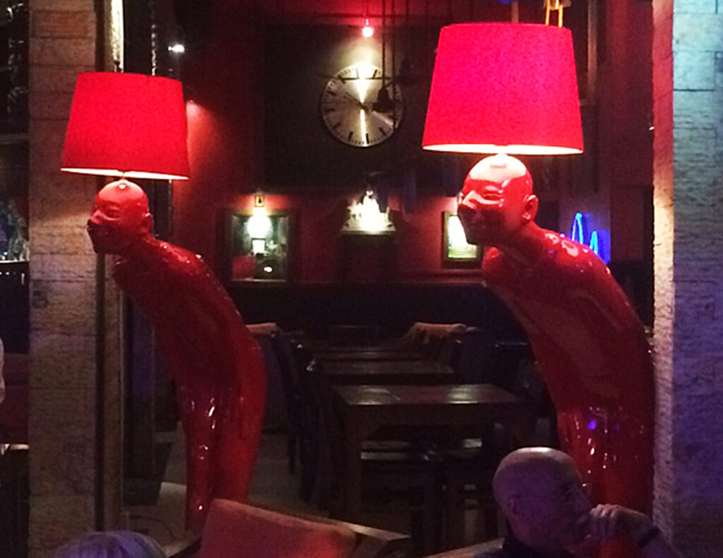 Red human figure sculptures with lampshades as heads in dimly-lit restaurant with tables and chairs.