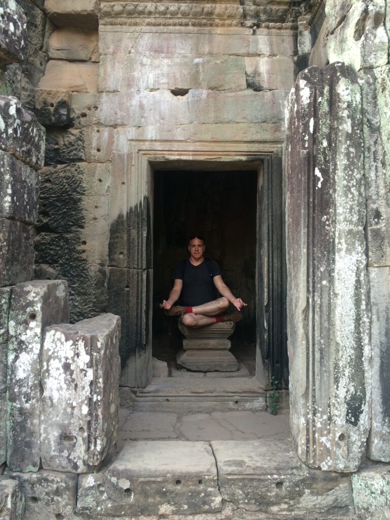 Person meditating cross-legged on stone pedestal in ancient stone structure with weathered blocks.