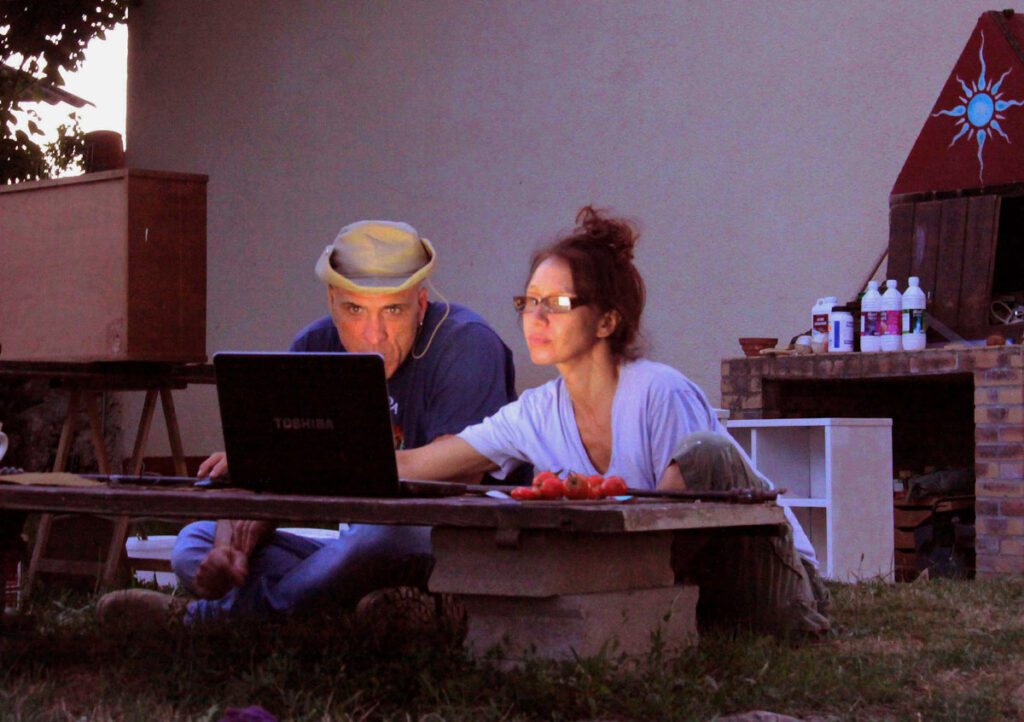 Two people seated outdoors with a Toshiba laptop on a low table, surrounded by various items.