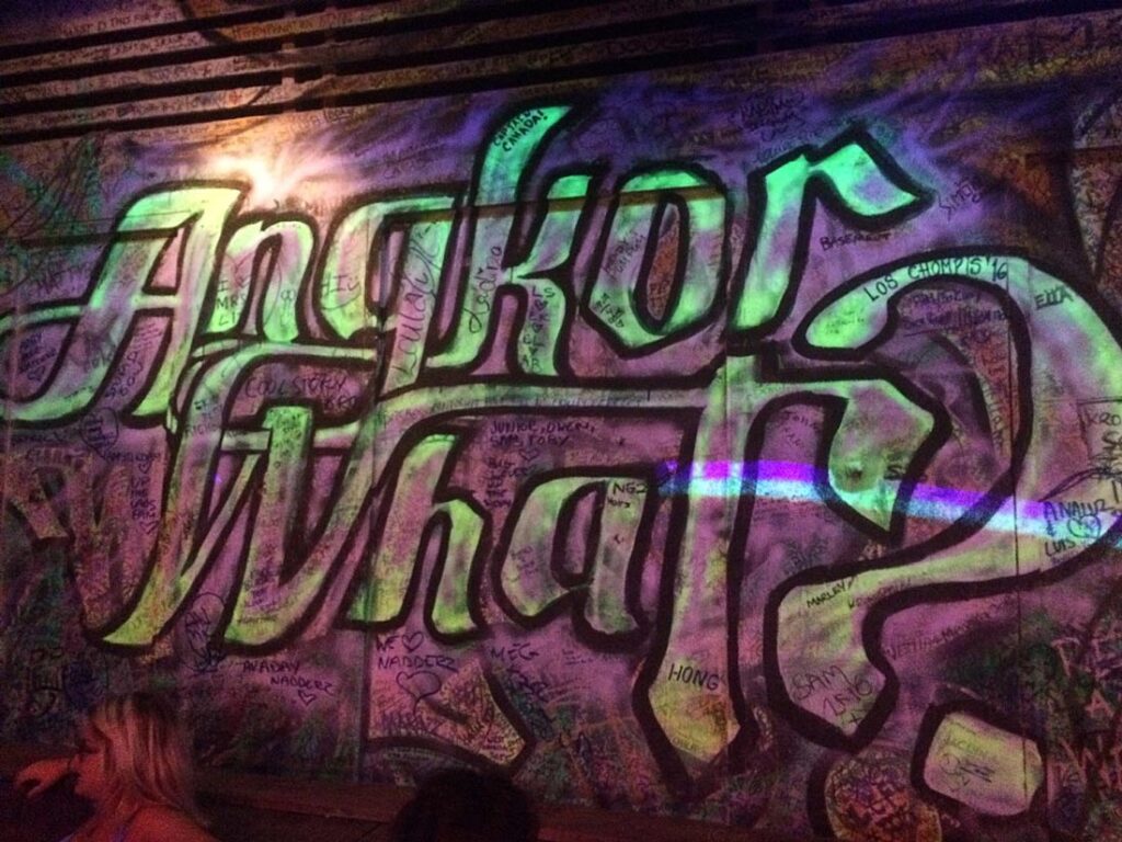 Colorful graffiti wall with large green letters "Anchor Wat" and numerous smaller inscriptions, doodles