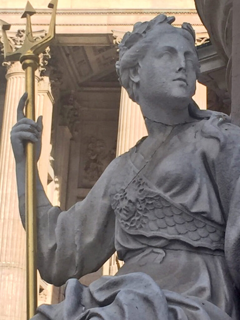 A stone sculpture of "Britannia" (Great Britain) in robes and wearing an olive-leaf crown while holding a gold trident sits outside the entrance to St Paul's Cathedral in London.