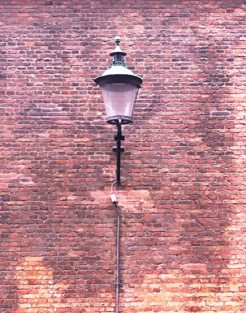 Old-fashioned street lamp on a worn, discolored brick wall with a cable extending below.