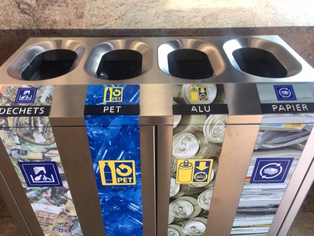 Recycling station with bins for general waste, plastic bottles, aluminum cans, and paper.