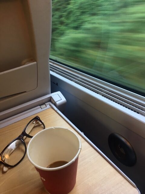 View from a window seat inside a high-speed European train with the service tray pulled down and the scenery outside whizzing by.