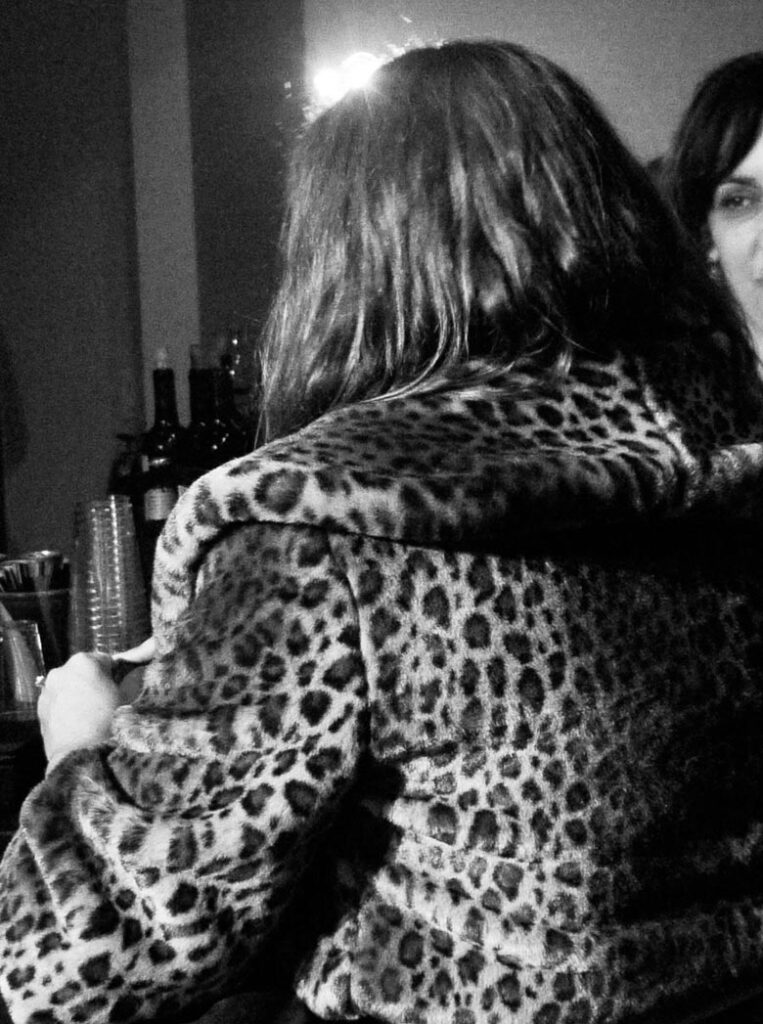 Black & white photo by Grace McEvoy of a woman (back turned) sitting at a bar in a leopard print jacket.