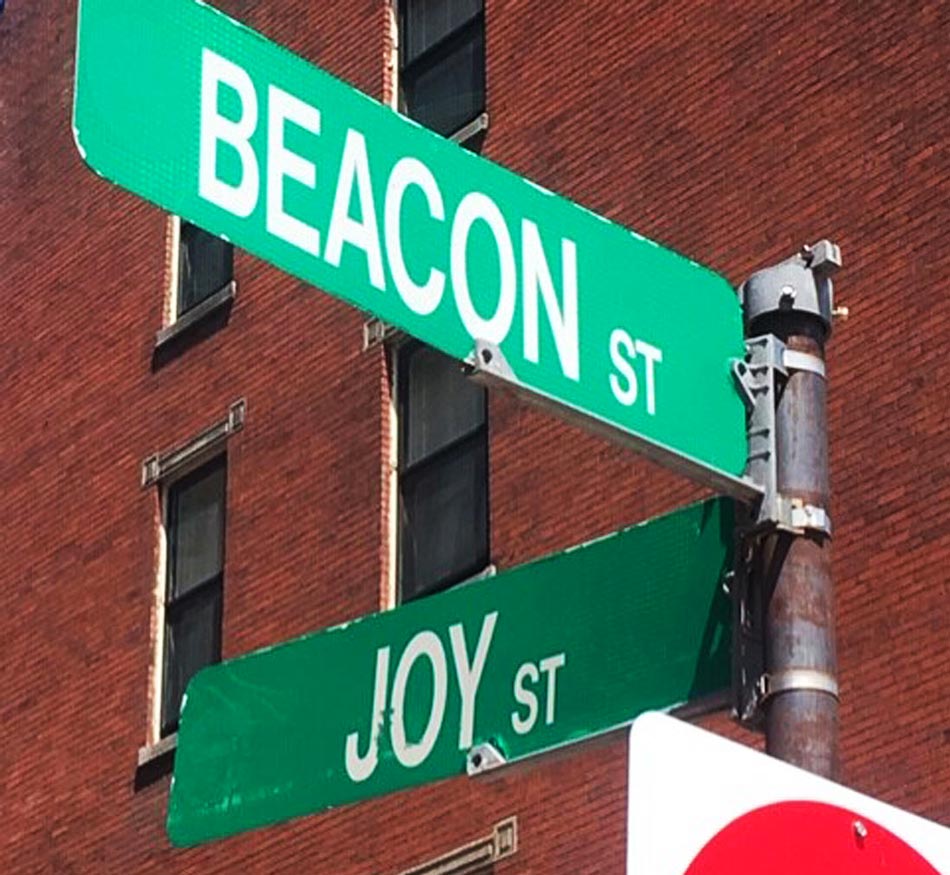 Green street sign with white lettering on a metal pole for the intersection of Beacon Street & Joy Street in Boston.