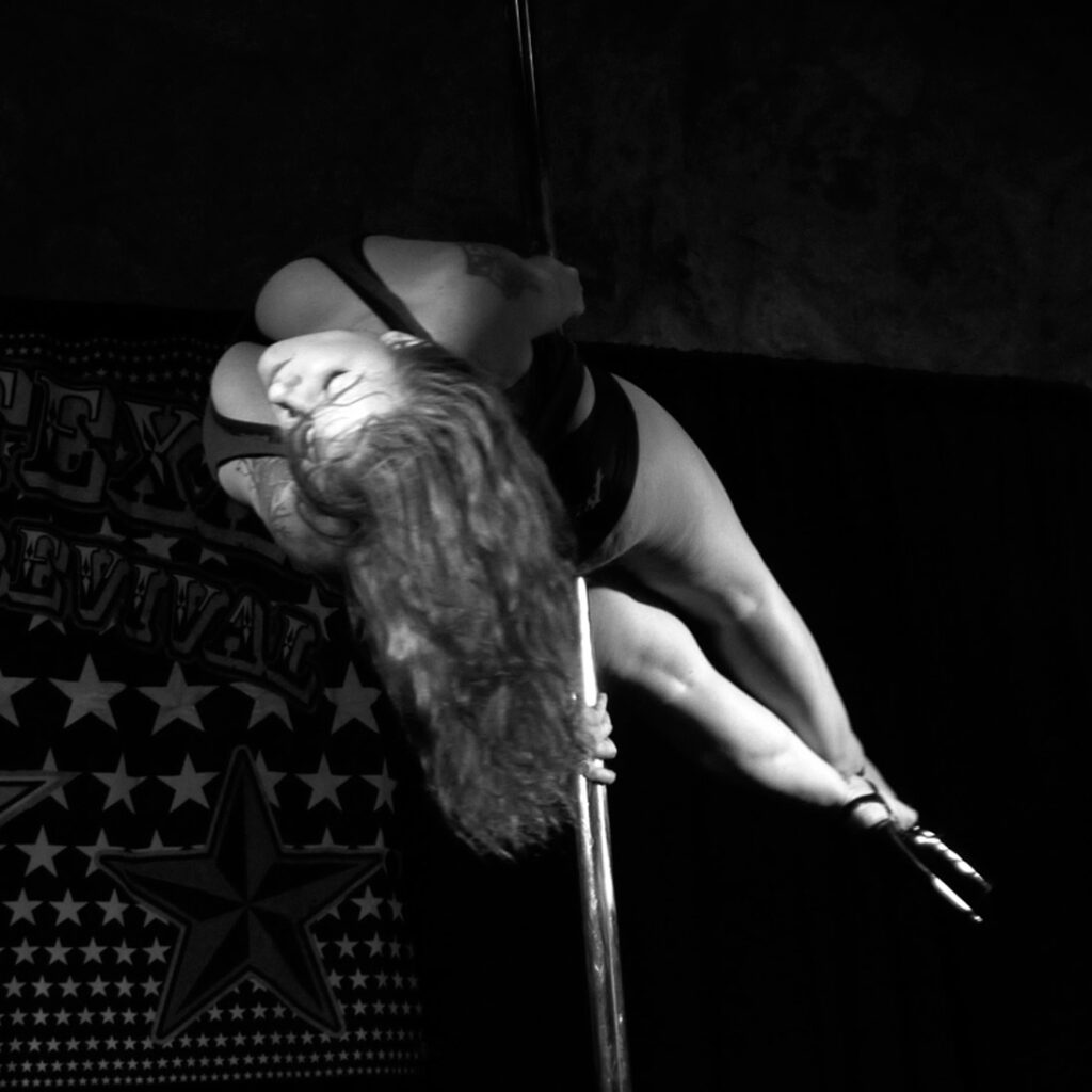 Black & white photo by Grace McEvoy of an erotic female dancer spinning horizontally on a pole.
