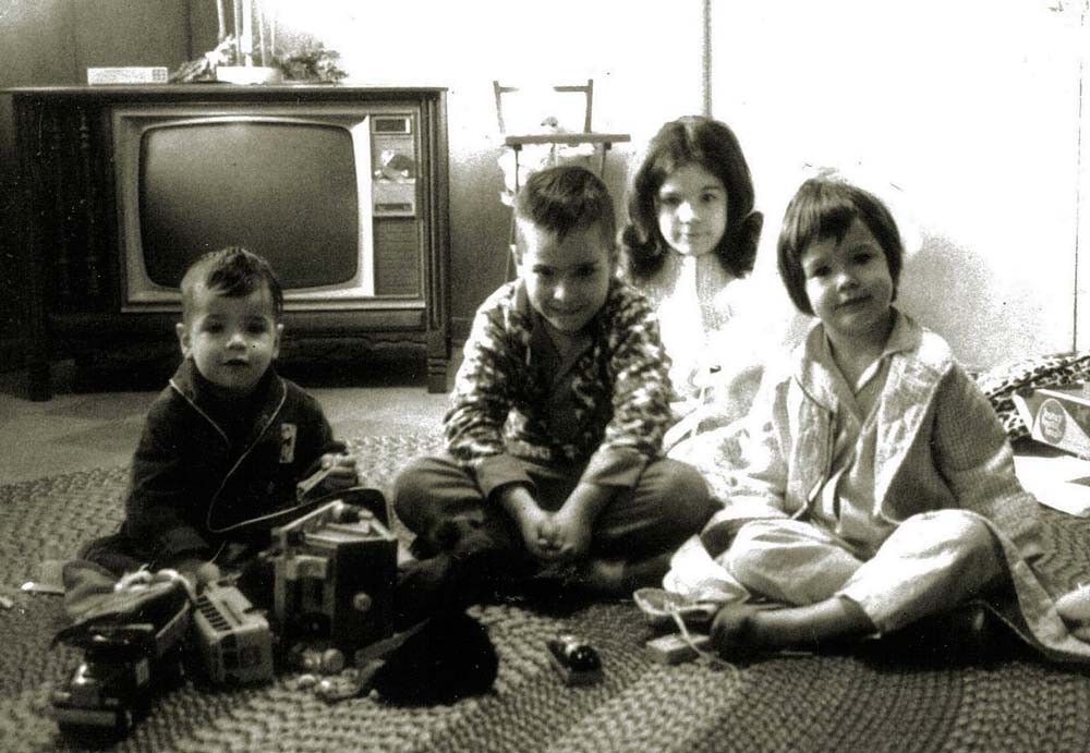 Vintage black & white photo of Ralph Williams as a child, age 7, sitting on the floor with his siblings on Christmas Day (L to R: Paul, Ralph, Ellen, Jennifer).