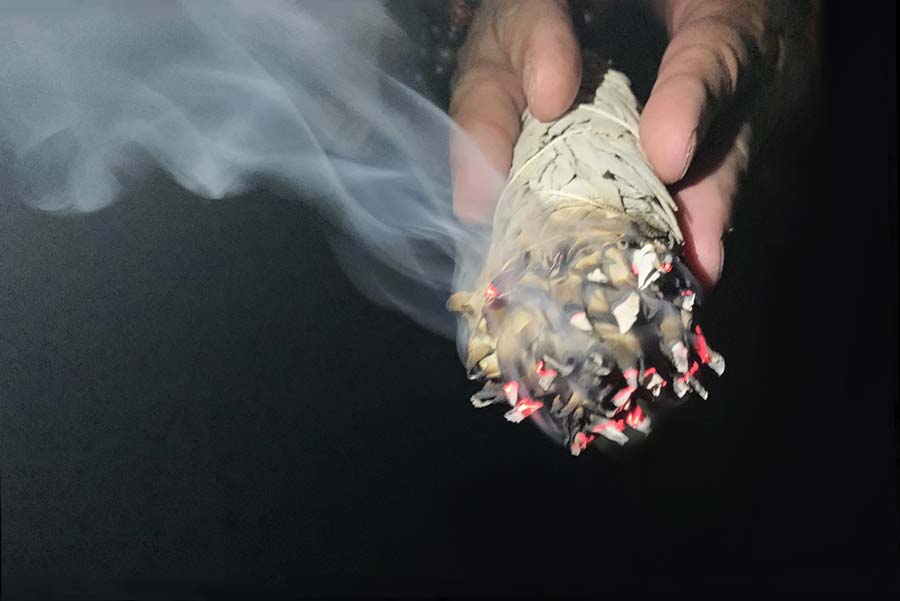 Two hands hold a bundle of burning sage at night.