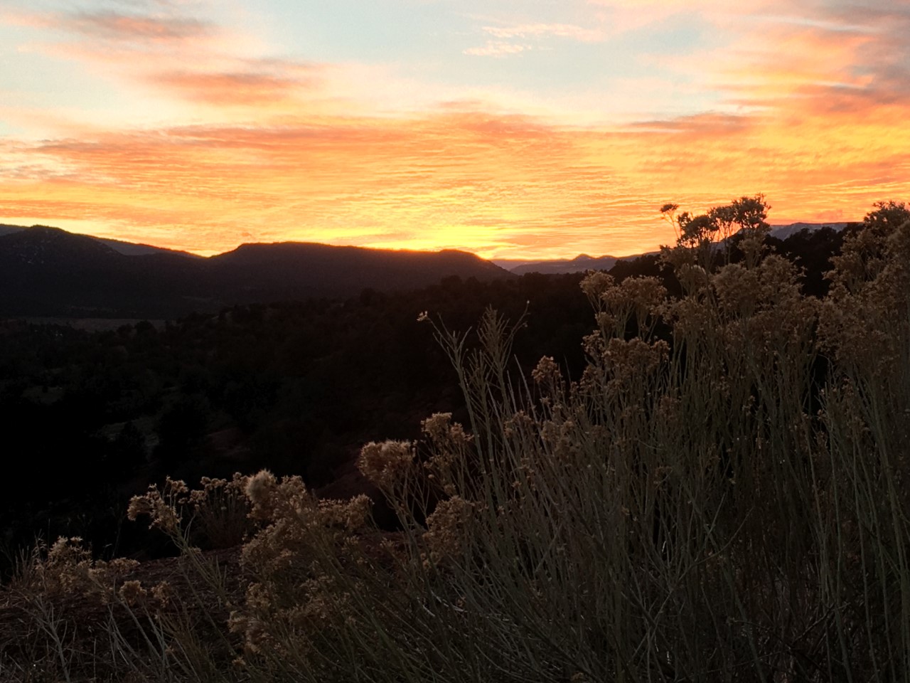 A blazing-orange sunset with rippling clouds glows brightly above distant mountains.