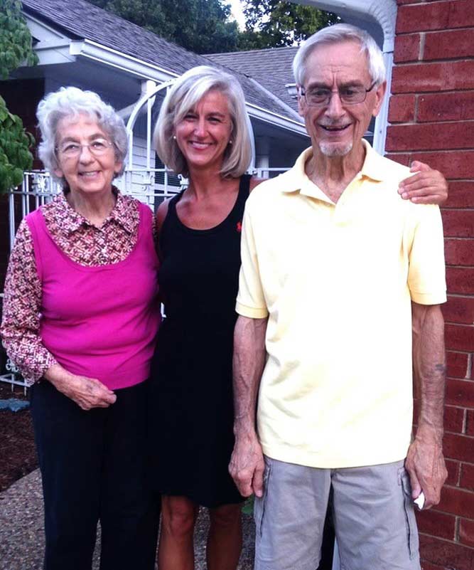 Dana Brock (center) smiles as she stands with her arms around her parents (on either side of her) outside their home in Bartlesville, Oklahoma (c. 2012).