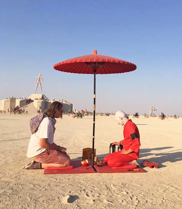 Hunter Horsfall sits under a red Asian-style umbrella with a bald Japanese man who is conducting a tea ceremony at the "Burning Man" festival in the Nevada desert.