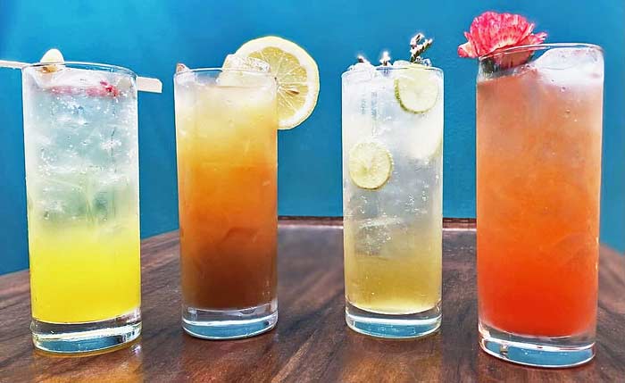 Four different sake cocktails with different garnishes are lined up on a bar, side by side.