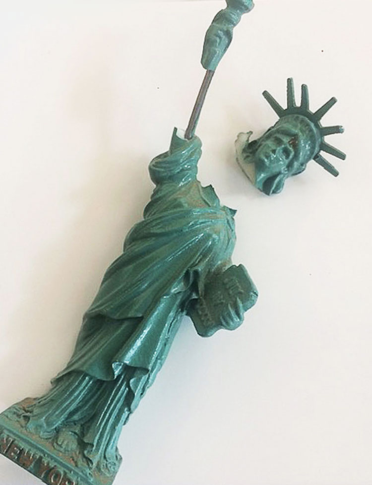 A small broken Statue of Liberty replica, head and torch detached, with "New York" inscription.