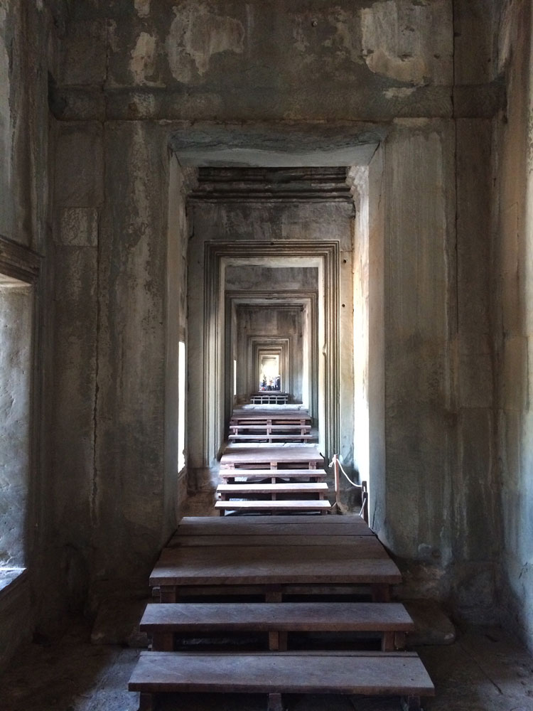 Long aged stone hallway with wooden steps and multiple doorways creating a perspective view.