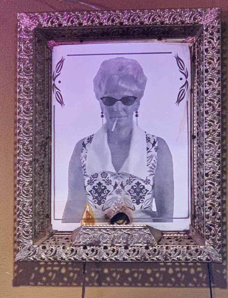 Black and white portrait of a person with sunglasses, cigarette, ornate frame, and small decorative items.