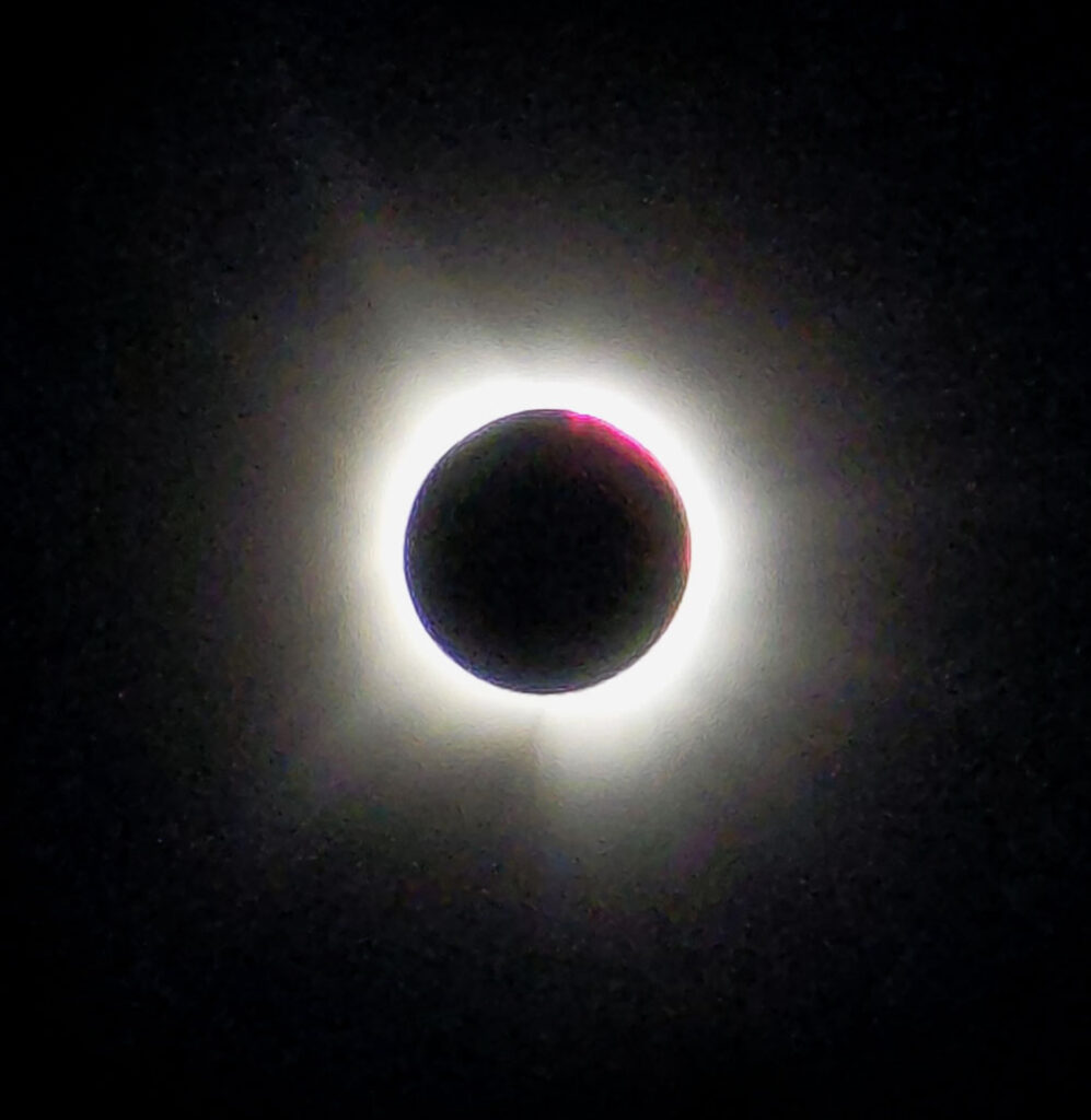 Solar eclipse with the moon covering the sun, revealing a bright corona and solar prominences.