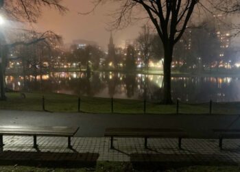 Boston Public Garden trinkles on a misty moody evening with the steeple of Arlington Street Church in silhouette in the distance.