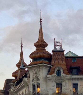 An elaborate red roof with spires is silhouetted against a dimming pastel sky in Geneva, Switzerland.